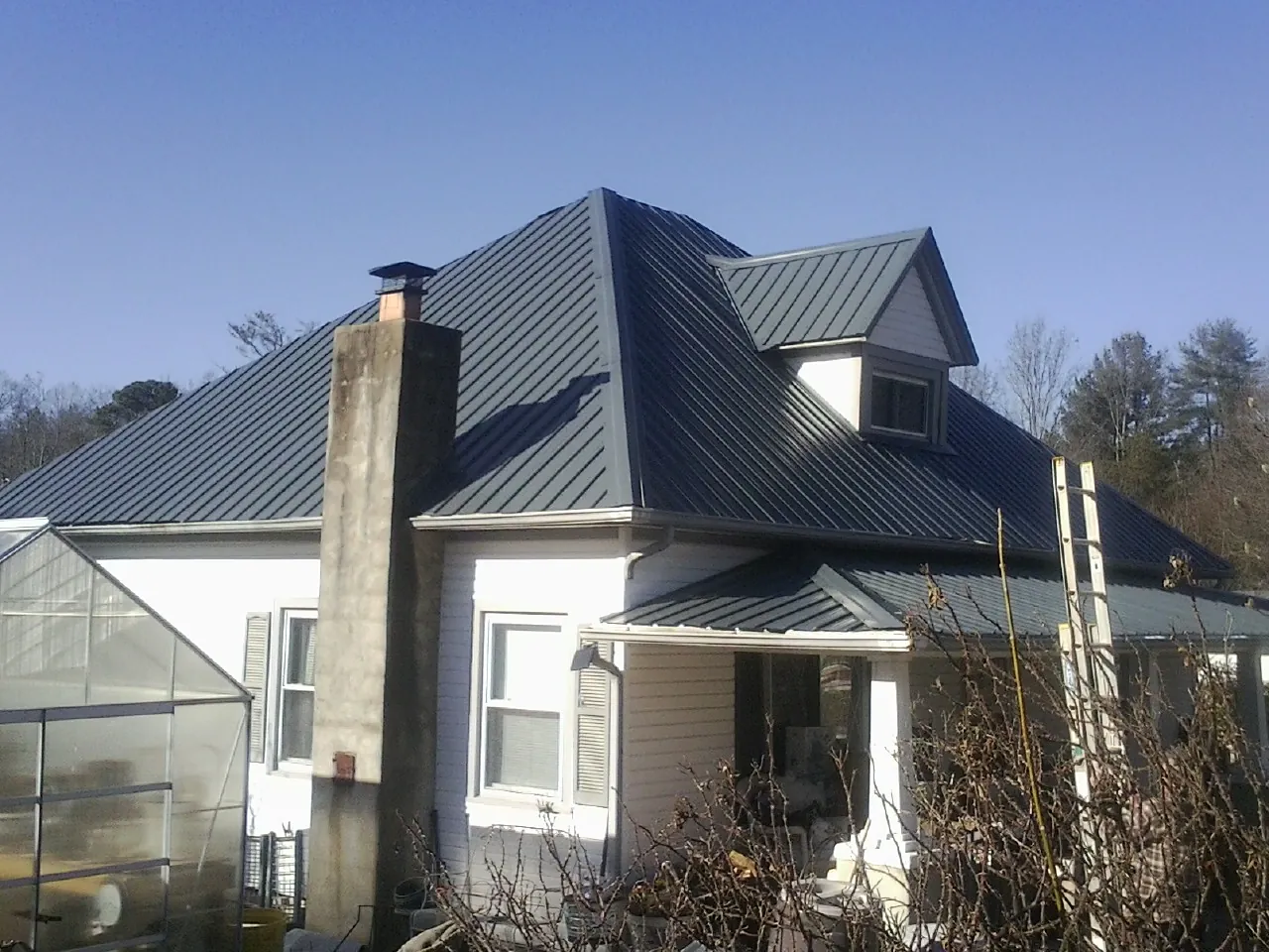 Dark blue standing seam metal roof on a white farmhouse with dormer — Slate & Tile Roof Repair by Roofing Brothers in New Straitsville