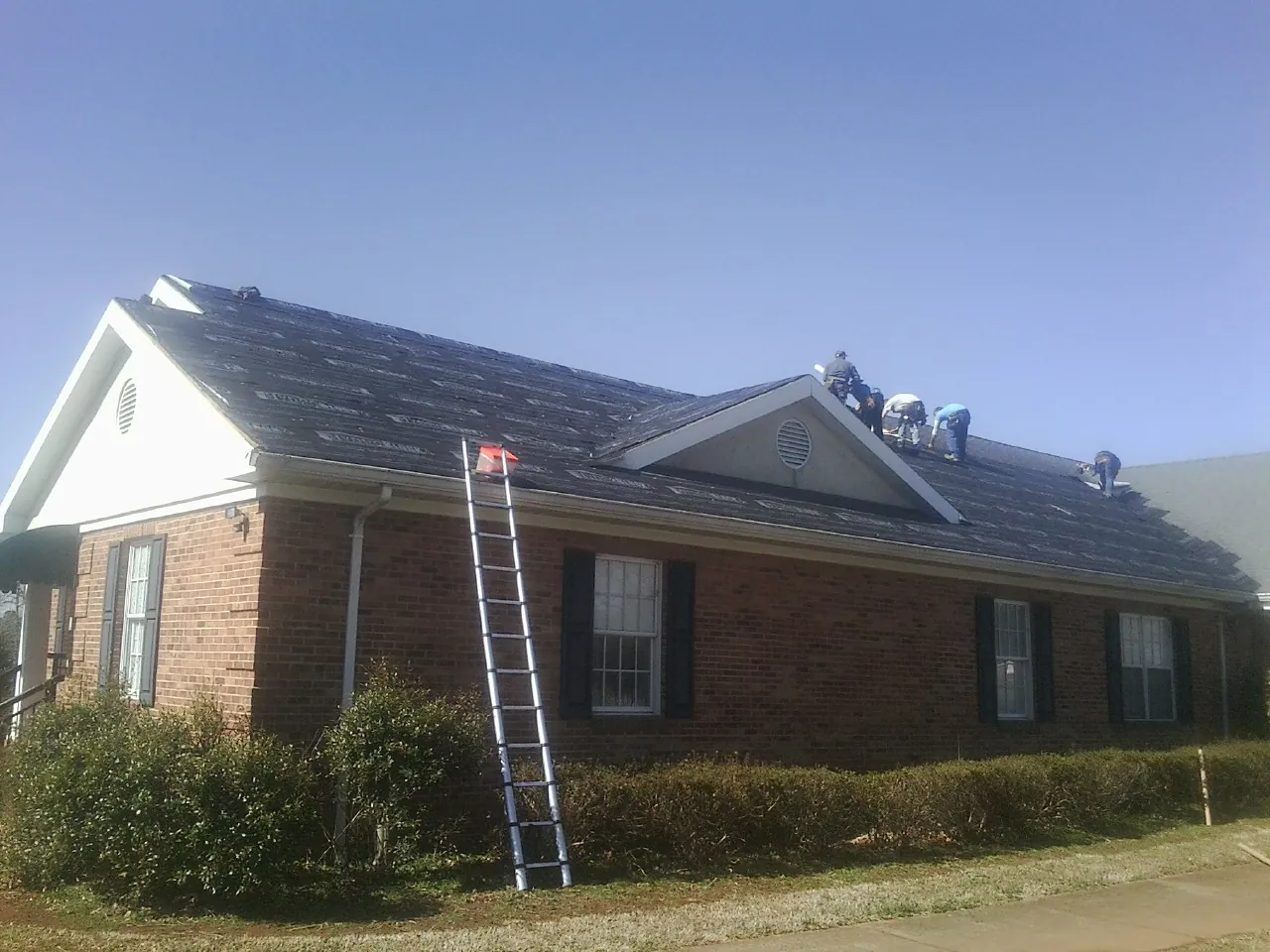 Crew tearing shingles off a brick ranch roof with a ladder set — Metal Roof Repair work by our crew in New Straitsville
