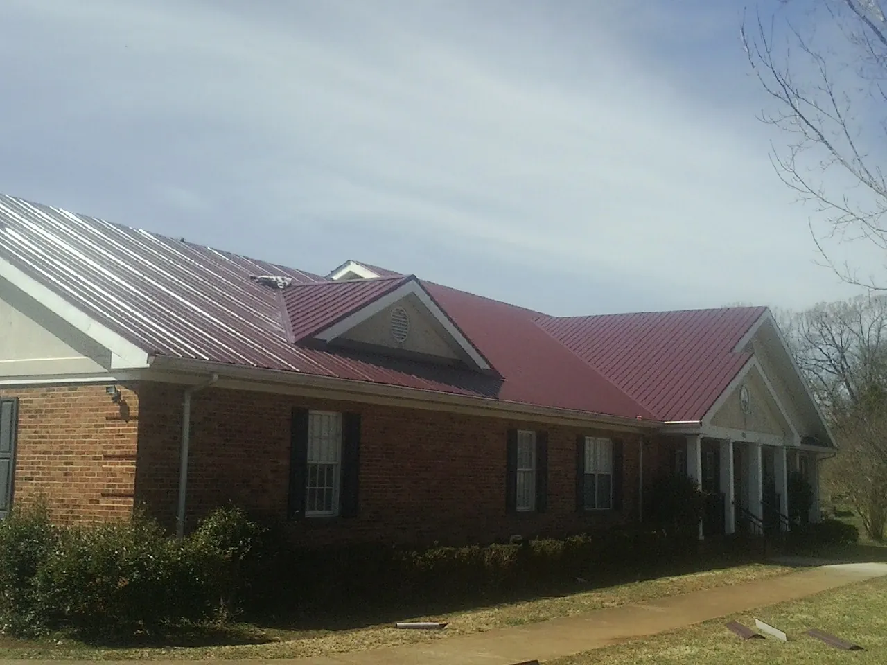 Red metal roof with gabled entries on a long brick building, from a Hail Damage Roof Repair job in New Straitsville