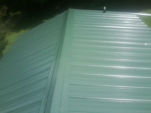 New green metal panels meeting at the ridge of a roof — Flat Roof Repair work by our crew in New Straitsville