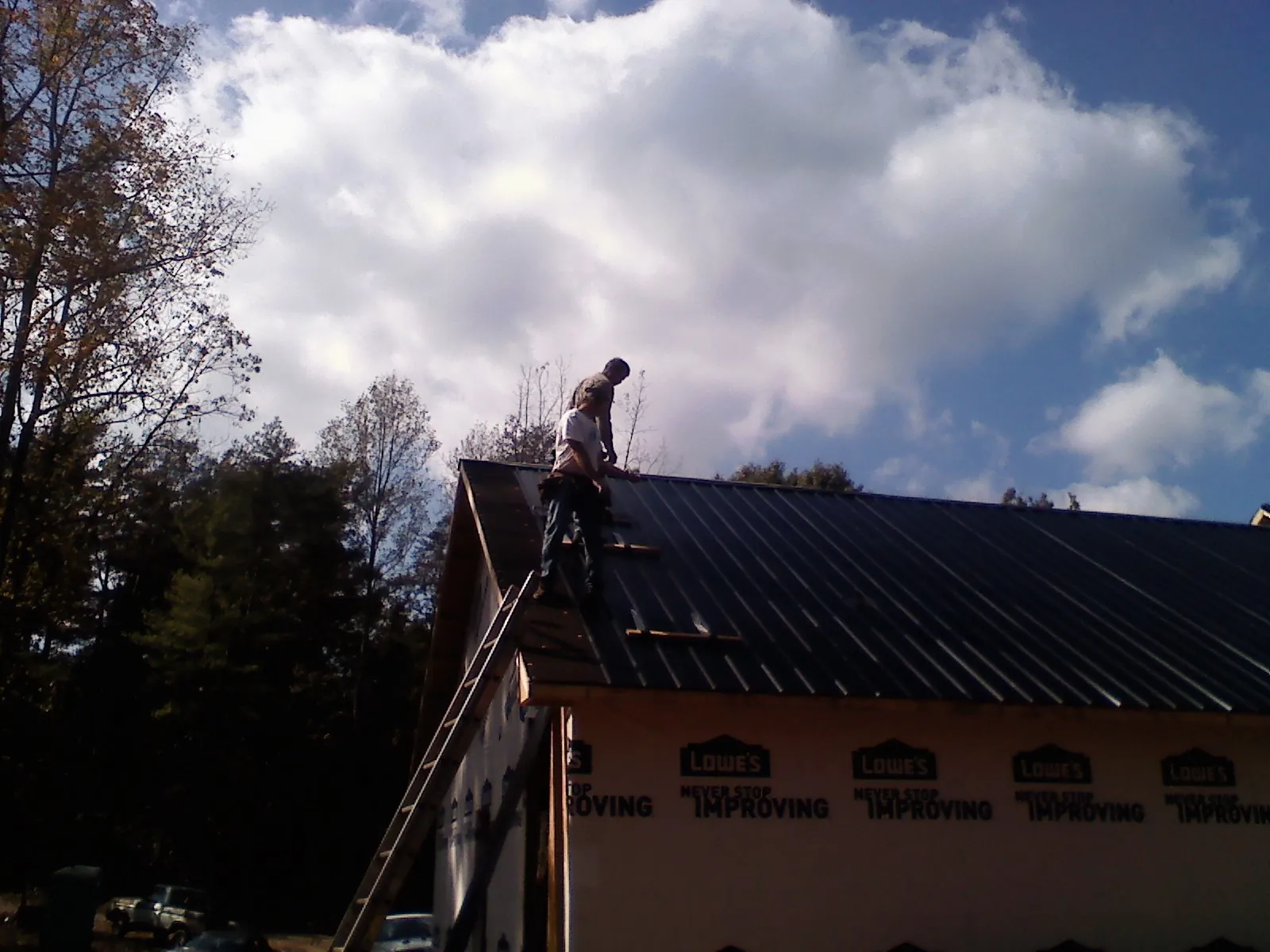 Roofer fastening dark metal panels high against a cloudy sky, from a Roof Inspection job in New Straitsville