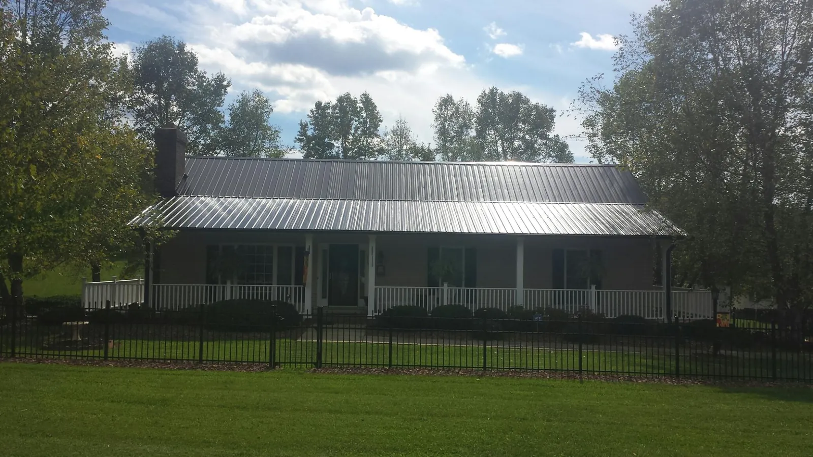 Gray metal roof on a brick ranch with a full width front porch — Gutter Guard Installation work by our crew in New Straitsville