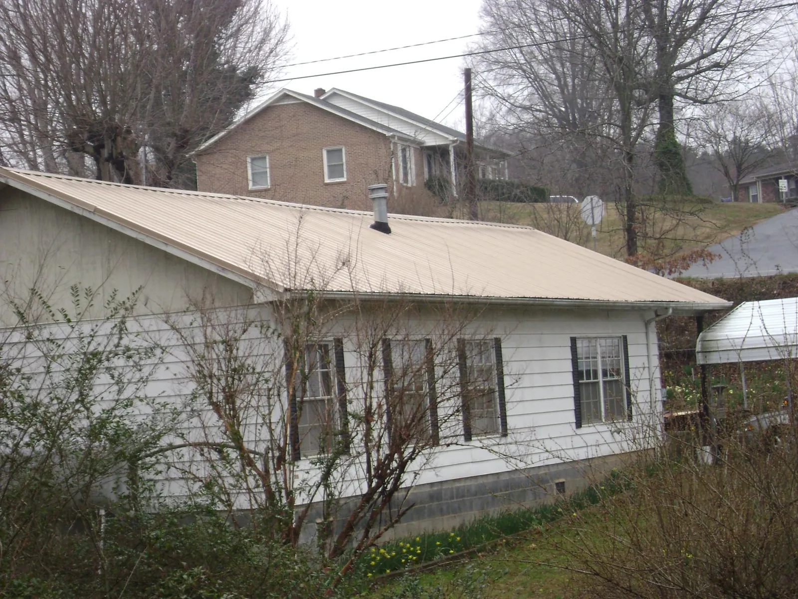 Tan metal roof on a white sided house set into a hillside — Commercial Roofing by Roofing Brothers in New Straitsville